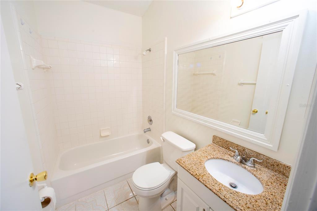 A bathroom featuring a white tub-shower combo, a toilet, and a granite-topped vanity — 1033 HAMLET DRIVE, MAITLAND, FL