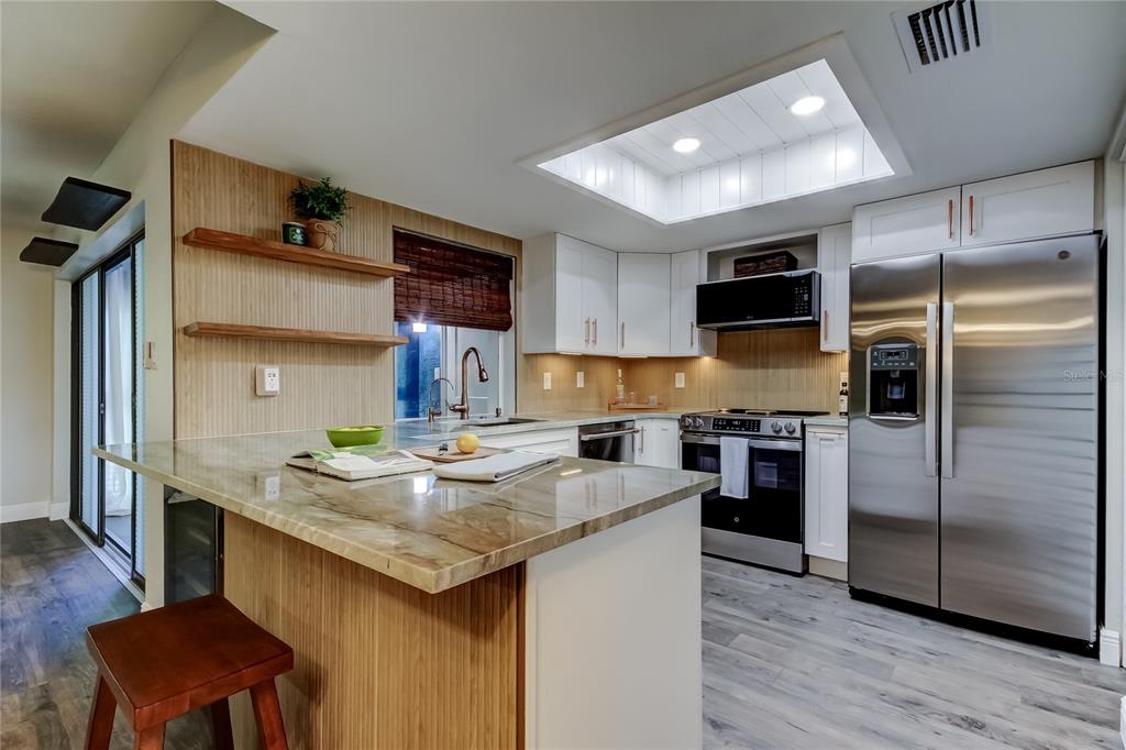 A kitchen with wood-paneled walls, white cabinets, stainless steel appliances, and a stone-topped island — 2673 SABAL SPRINGS CIRCLE UNIT 201, CLEARWATER, FL