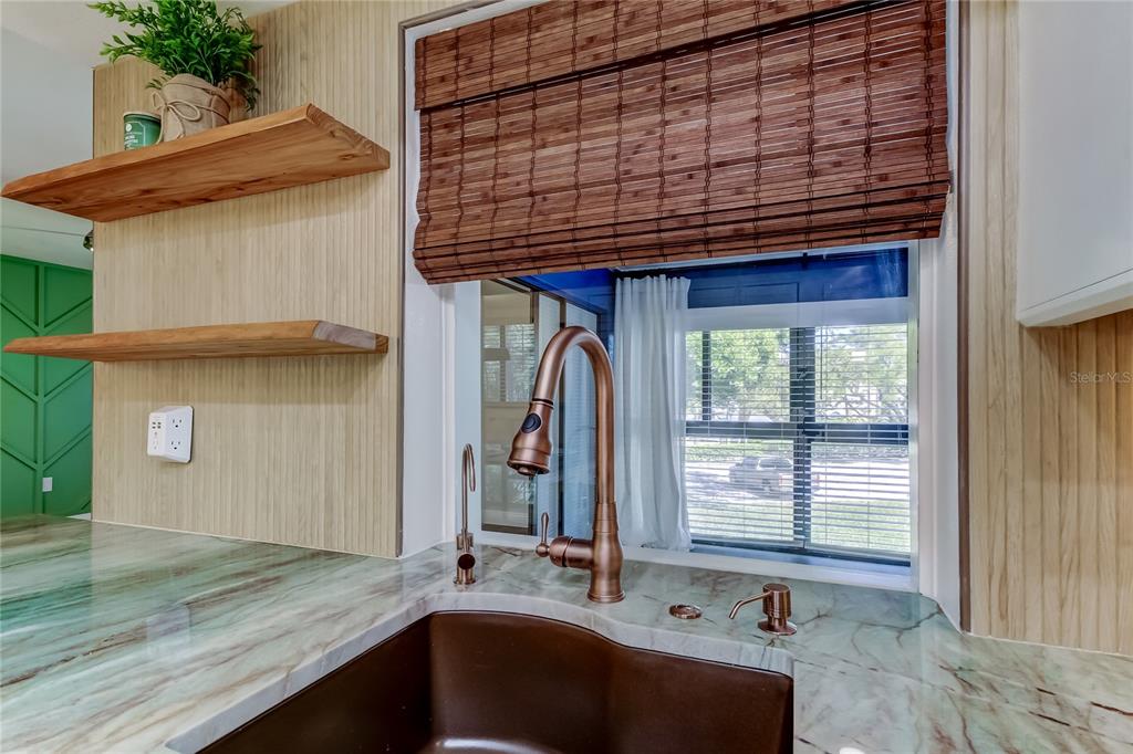 A kitchen sink area features a copper faucet, marble-look countertop, and natural wood shelving — 2673 SABAL SPRINGS CIRCLE UNIT 201, CLEARWATER, FL
