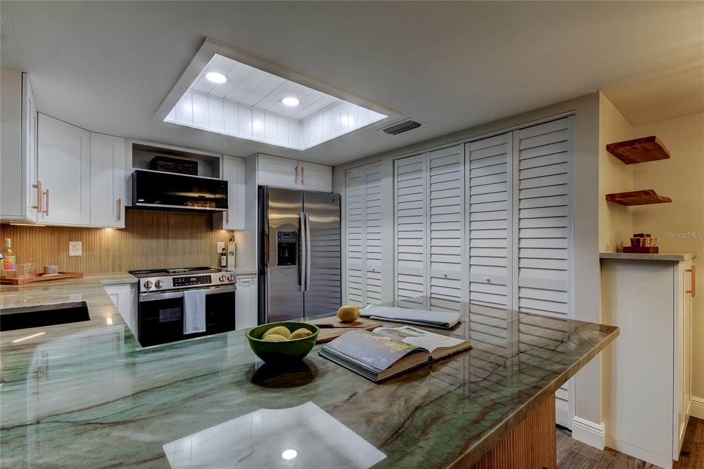 A kitchen features white cabinetry, stainless steel appliances, and a green-veined stone countertop island — 2673 SABAL SPRINGS CIRCLE UNIT 201, CLEARWATER, FL