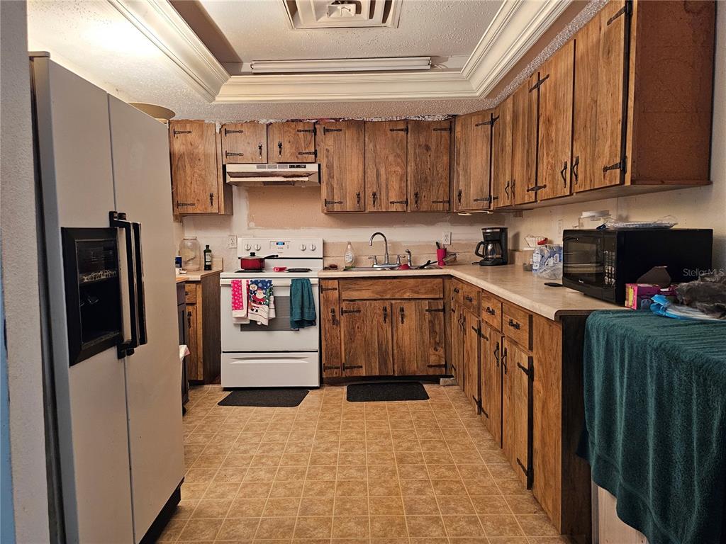A kitchen features wood cabinets, white appliances, laminate countertops, and a tiled floor — 320 COUNTY ROAD 619, LAKE PLACID, FL