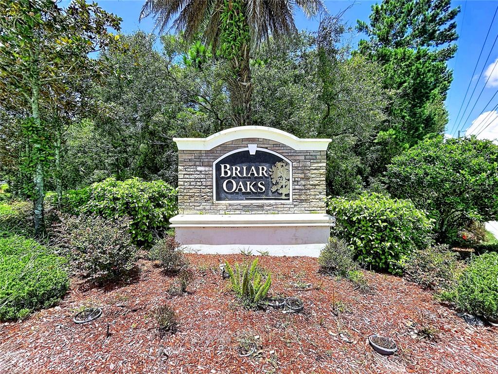 A stone monument sign for Briar Oaks stands in a landscaped garden with trees — 18607 BRIAR OAKS DRIVE, HUDSON, FL