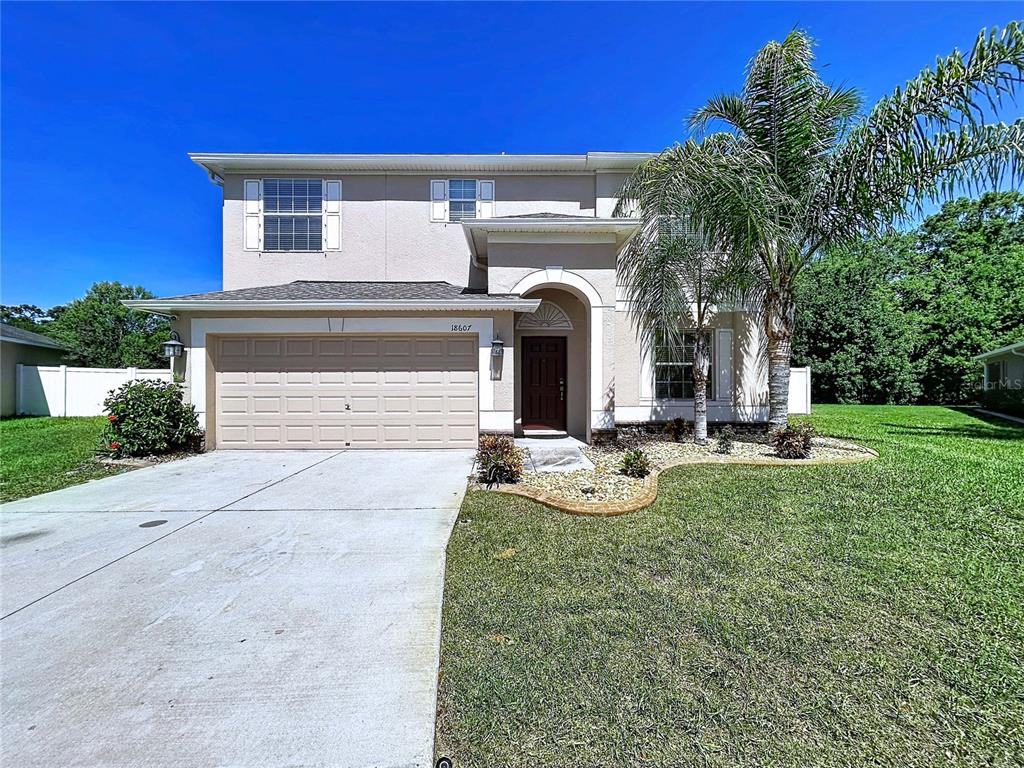 A two-story suburban house with a tan stucco exterior, a two-car garage, and a palm tree — 18607 BRIAR OAKS DRIVE, HUDSON, FL