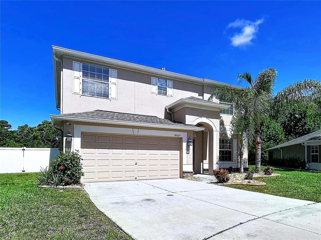 A two-story suburban house features a beige stucco exterior, a two-car garage, and a palm tree — 18607 BRIAR OAKS DRIVE, HUDSON, FL