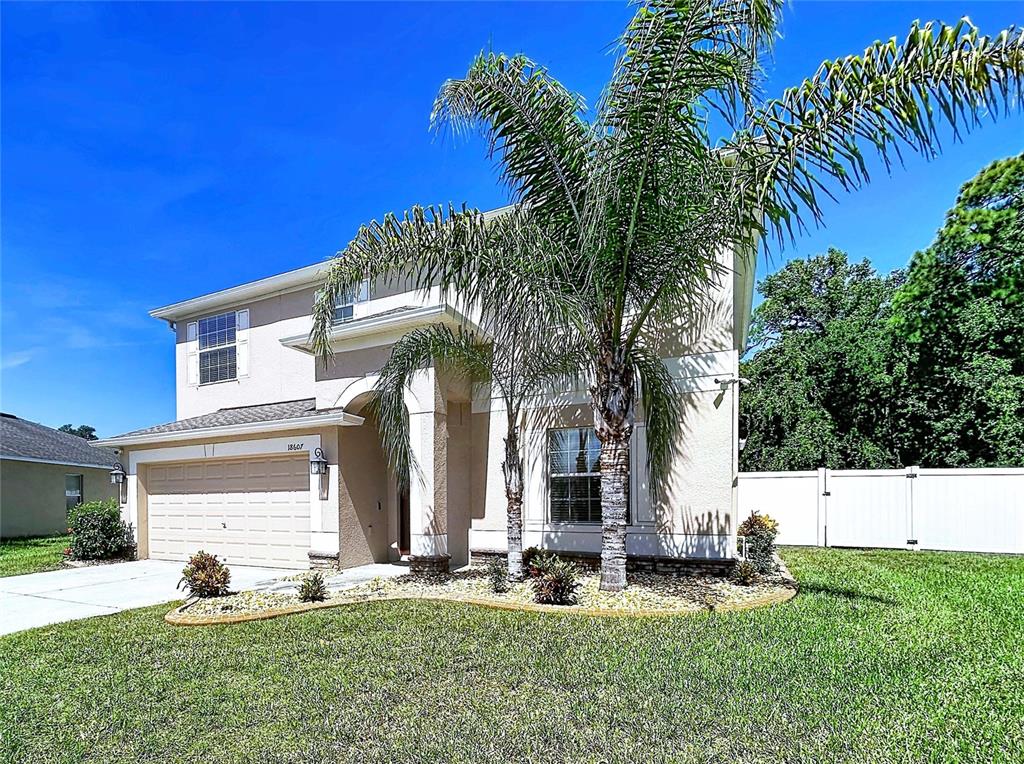 A two-story suburban house with a beige exterior, a two-car garage, and a palm tree — 18607 BRIAR OAKS DRIVE, HUDSON, FL