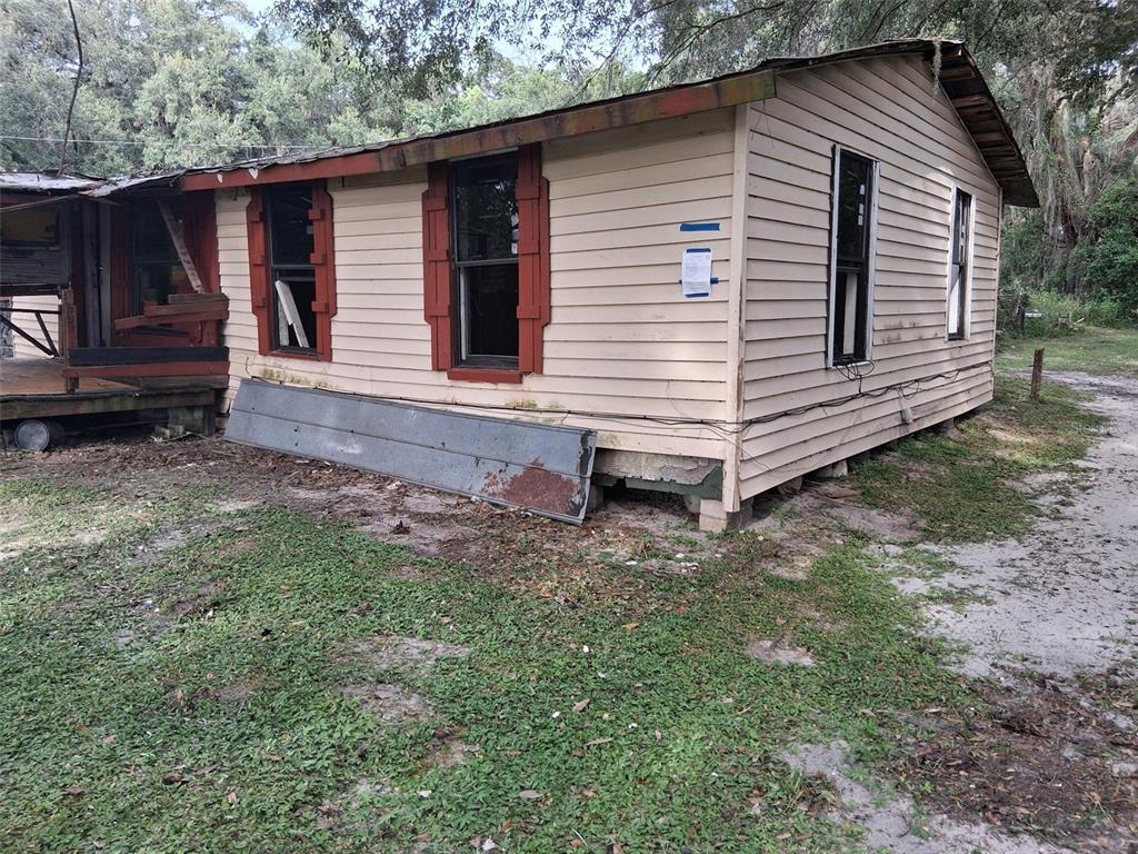 A weathered, single-story house with light siding and red window shutters sits on a dirt lot — 18255 NW 60TH AVENUE, REDDICK, FL