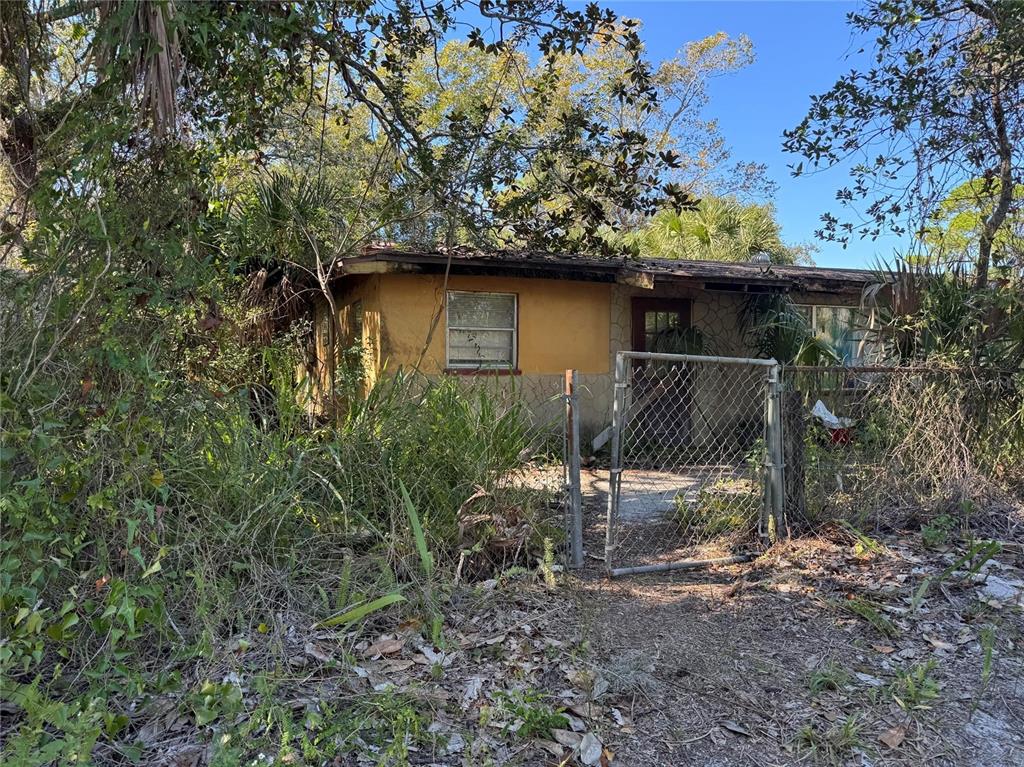 A weathered, single-story house with yellow stucco walls stands behind a chain-link fence — 8153 OAKLEAF AVENUE, PORT RICHEY, FL