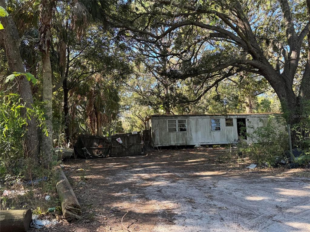 A weathered mobile home sits on a dirt lot surrounded by mature trees and vegetation — 8153 OAKLEAF AVENUE, PORT RICHEY, FL