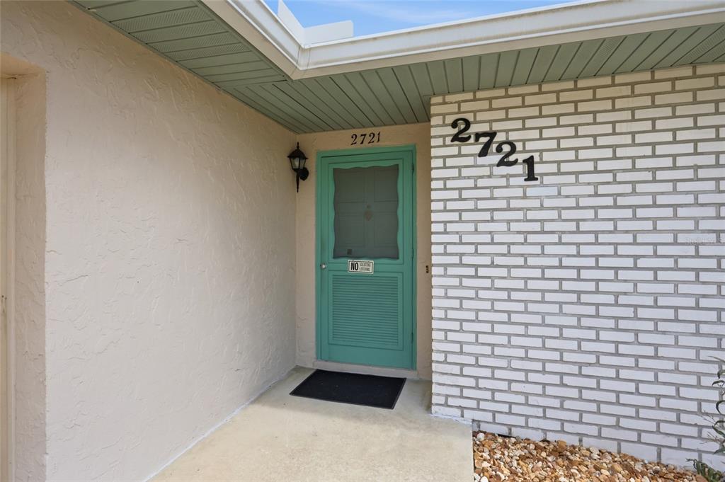 A teal front door is set between a white brick wall and a beige stucco wall — 2721 CECILE STREET, KISSIMMEE, FL