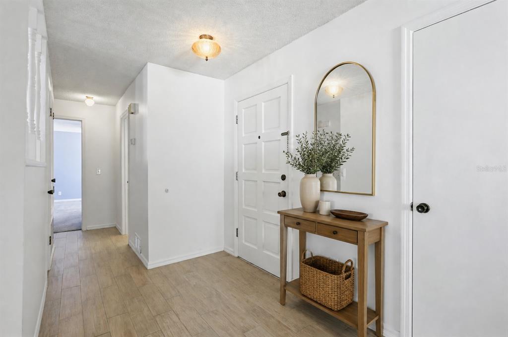 An entryway features light wood-look tile flooring, a white door, a console table, and a mirror — 2721 CECILE STREET, KISSIMMEE, FL