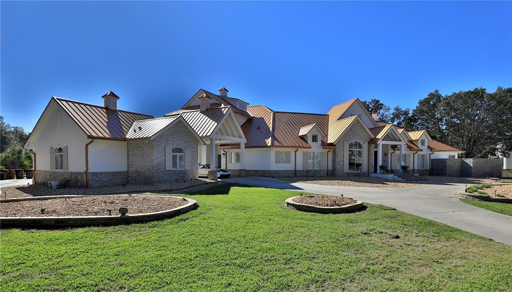 A large, single-story house with a metal roof, stone facade, and a paved driveway — 7387 SE 12TH CIRCLE, OCALA, FL