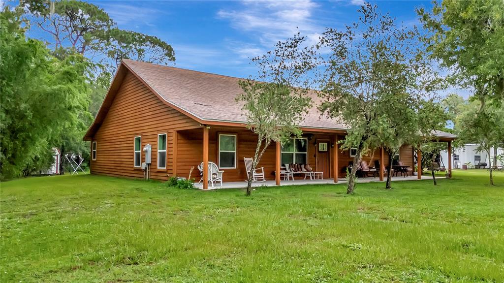 A brown wood-sided house with a covered porch sits on a grassy lot with trees — 7427 REDWING ROAD, GROVELAND, FL