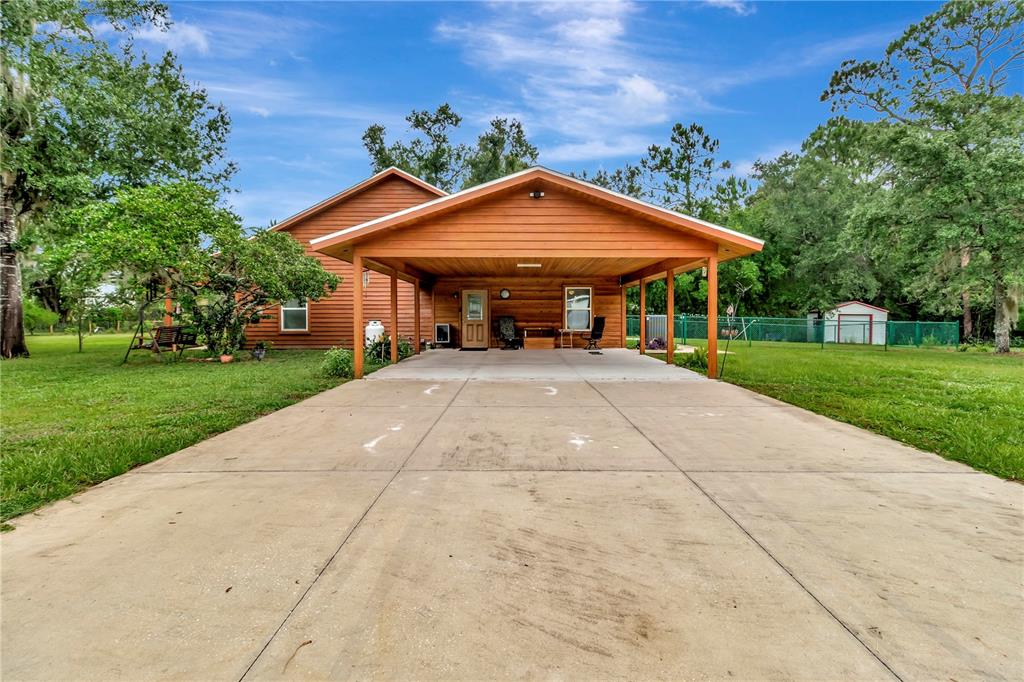 A wooden house with a large attached carport and a concrete driveway in a yard — 7427 REDWING ROAD, GROVELAND, FL
