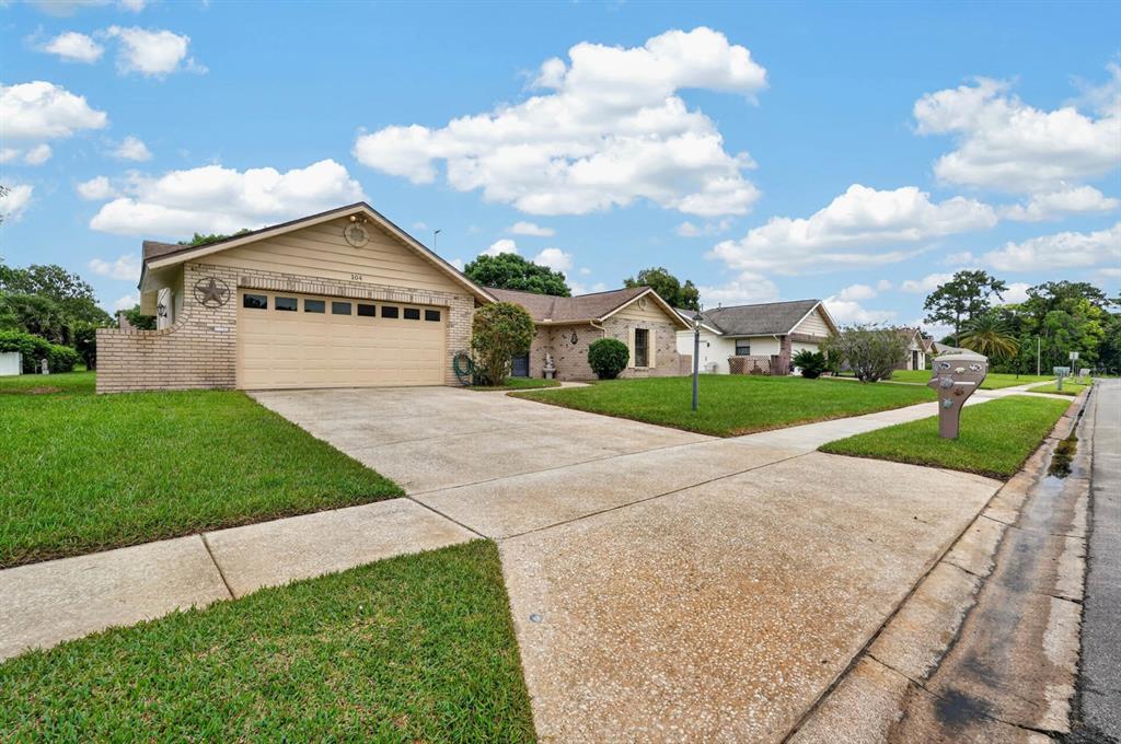 A single-story house with a beige garage and brick accents sits behind a concrete driveway — 104 COLLEEN DRIVE, DAYTONA BEACH, FL