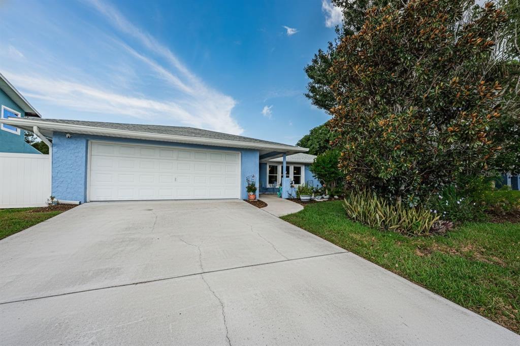 A light blue house with a two-car garage and a concrete driveway under a blue sky — 1886 ARGILE DRIVE, DUNEDIN, FL