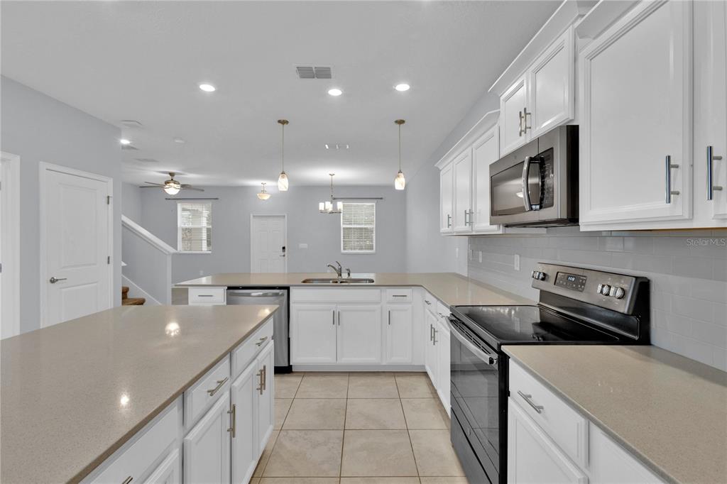 A kitchen with white cabinets, quartz countertops, stainless steel appliances, and tile flooring — 11048 SUSPENSE DRIVE, WINTER GARDEN, FL