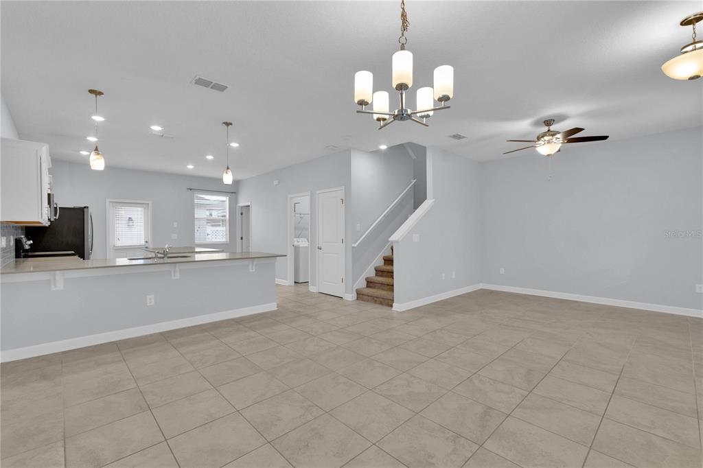 An open-concept living and kitchen area features tile flooring, a staircase, and a chandelier — 11048 SUSPENSE DRIVE, WINTER GARDEN, FL