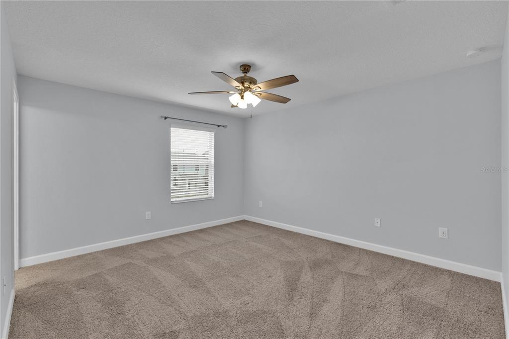 An empty bedroom features light gray walls, beige carpeting, and a ceiling fan — 11048 SUSPENSE DRIVE, WINTER GARDEN, FL