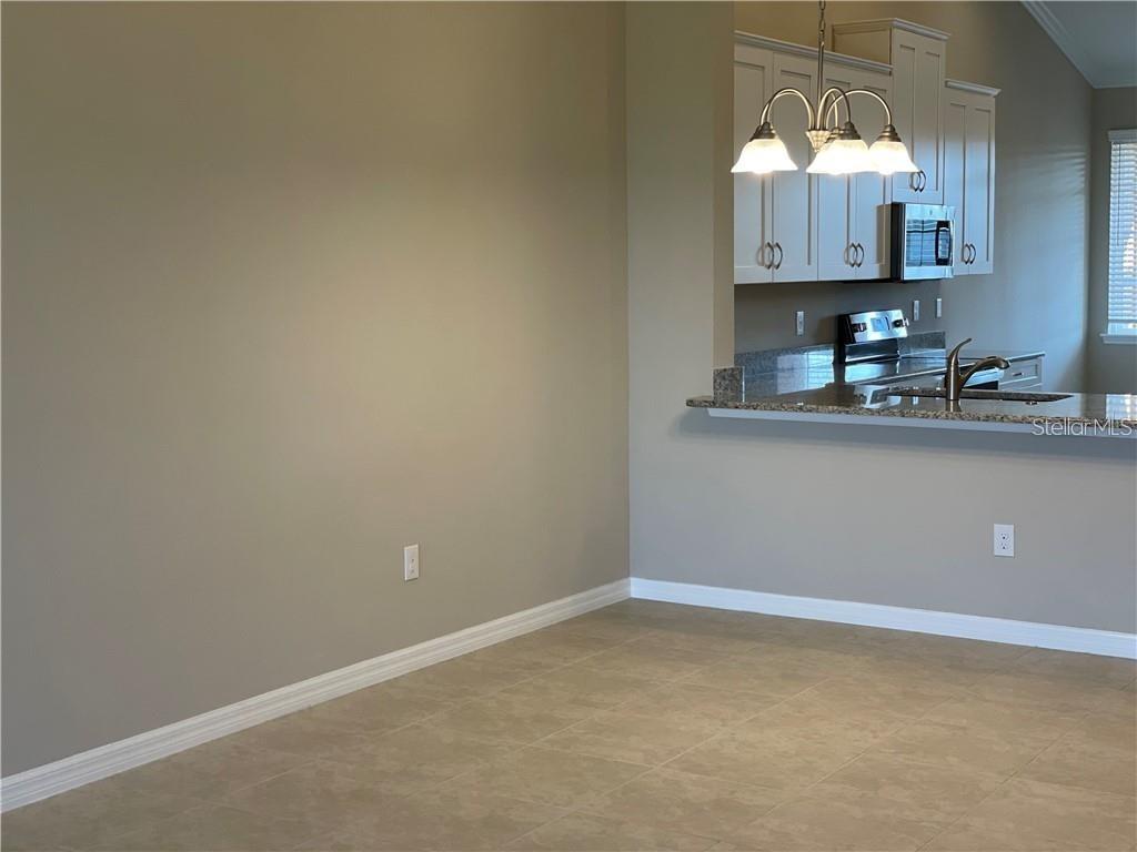 A dining area with tile flooring sits adjacent to a kitchen with white cabinets — 13823 MESSINA LOOP UNIT 203, BRADENTON, FL