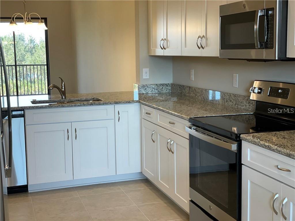 A kitchen features white cabinets, granite countertops, stainless steel appliances, and a window with blinds — 13823 MESSINA LOOP UNIT 203, BRADENTON, FL