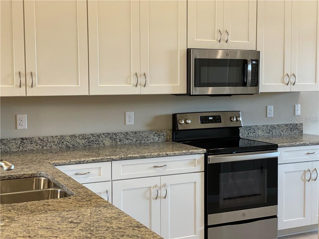 A kitchen features white cabinets, granite countertops, and stainless steel appliances — 13823 MESSINA LOOP UNIT 203, BRADENTON, FL