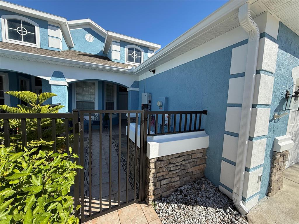 A blue stucco house exterior features a stone-accented wall, a metal gate, and a walkway — 3172 RIVER BRANCH CIRCLE, KISSIMMEE, FL
