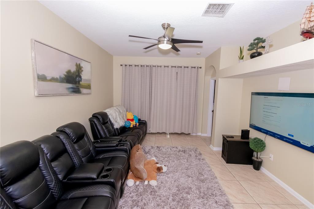 A living room features black leather reclining chairs, a gray area rug, and a wall-mounted television — 3172 RIVER BRANCH CIRCLE, KISSIMMEE, FL