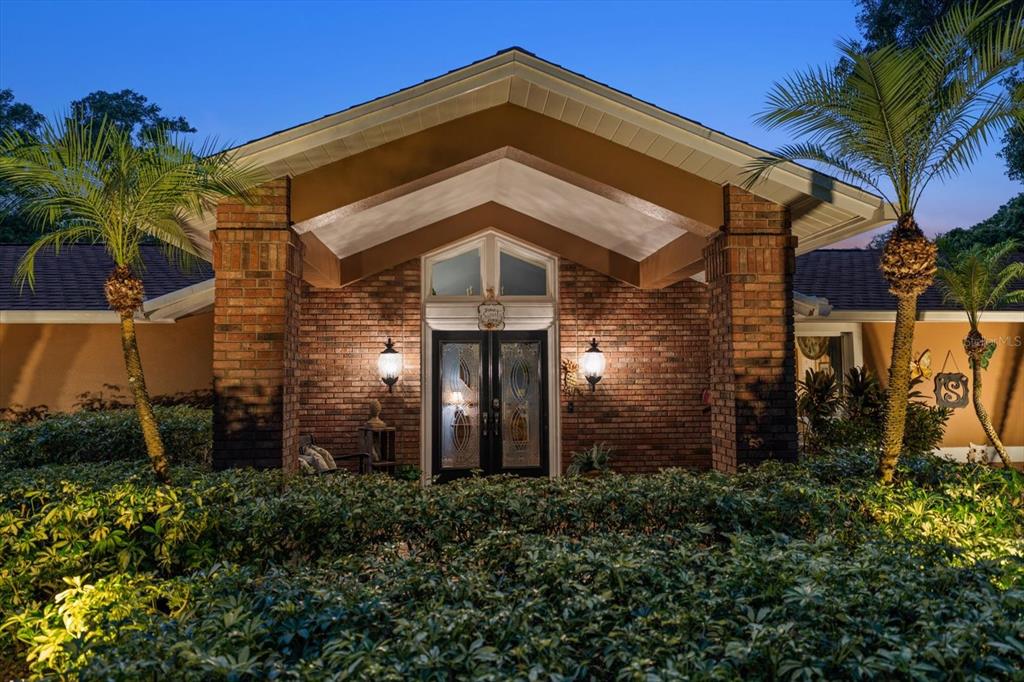 A brick house exterior features a covered entryway with double glass doors and palm trees — 4141 WINDING WILLOW DRIVE, PALM HARBOR, FL