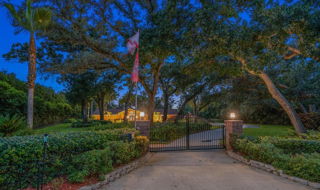 A gated driveway leads to a house surrounded by large trees at dusk — 4141 WINDING WILLOW DRIVE, PALM HARBOR, FL