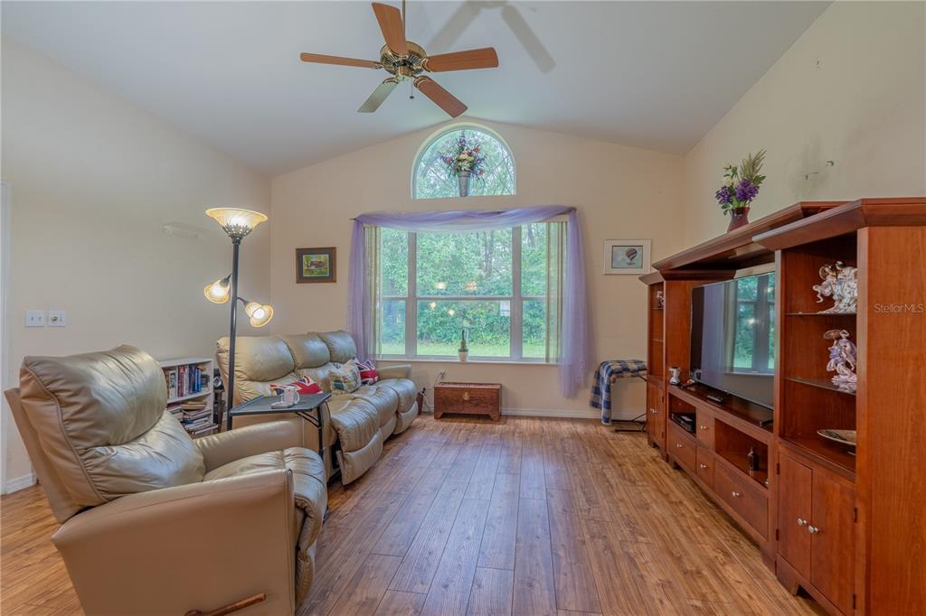 A living room features wood-look flooring, a vaulted ceiling with a fan, and a large window — 10971 SW 69TH CIRCLE, OCALA, FL