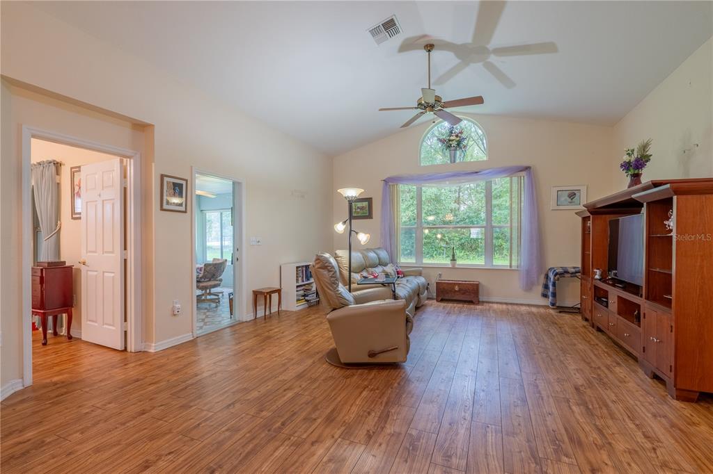 A living room with wood-look flooring, a vaulted ceiling, and a large window with drapes — 10971 SW 69TH CIRCLE, OCALA, FL