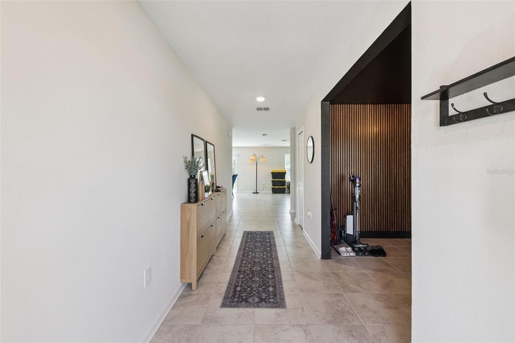 A tiled hallway leads to an open living area featuring a wood-slat accent wall — 5478 LIMESTONE STREET, MOUNT DORA, FL