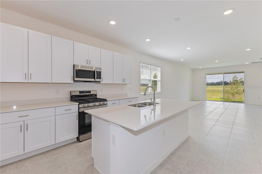 A modern kitchen features white cabinets, stainless steel appliances, a center island, and tile flooring — 9120 WILDLIGHT TRAIL, WILDWOOD, FL