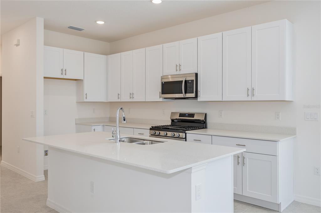A modern kitchen features white cabinets, a large island with a sink, and stainless appliances — 9120 WILDLIGHT TRAIL, WILDWOOD, FL