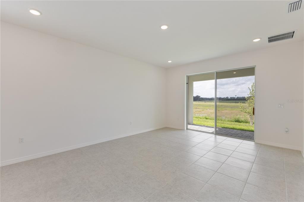An empty room with light-colored tile flooring, white walls, recessed lighting, and a sliding glass door — 9120 WILDLIGHT TRAIL, WILDWOOD, FL