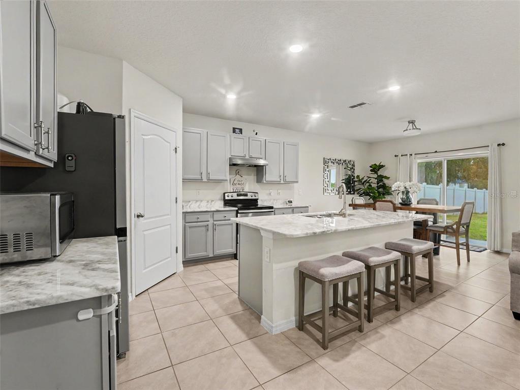 A kitchen features gray cabinets, a marble-topped island with three stools, and tile flooring — 210 MEADOWBROOK BOULEVARD, WINTER HAVEN, FL