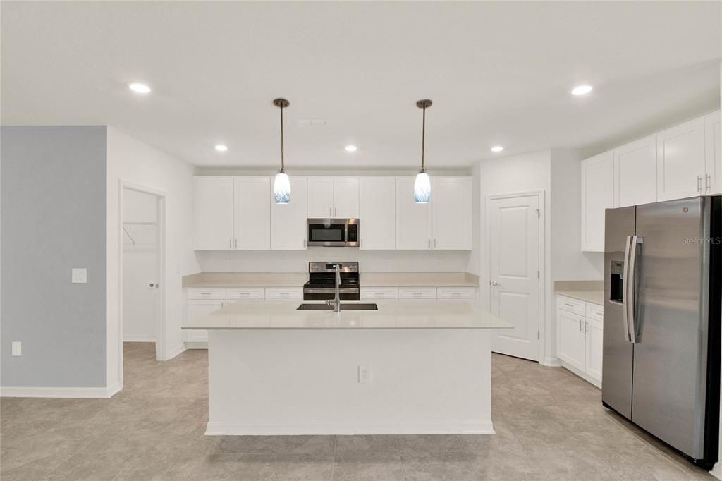 A modern kitchen features white cabinetry, a central island, stainless steel appliances, and tile flooring — 271 INMAN BOULEVARD, WINTER HAVEN, FL