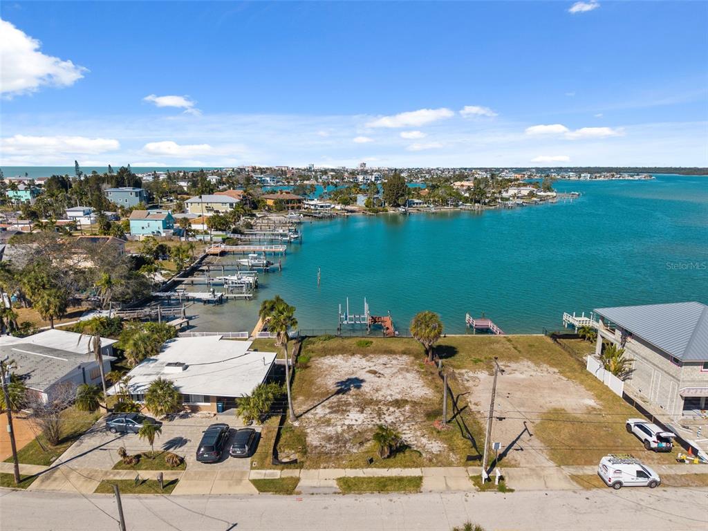 An aerial view shows two vacant waterfront lots with docks and nearby residential houses — 15307 HARBOR DRIVE, MADEIRA BEACH, FL