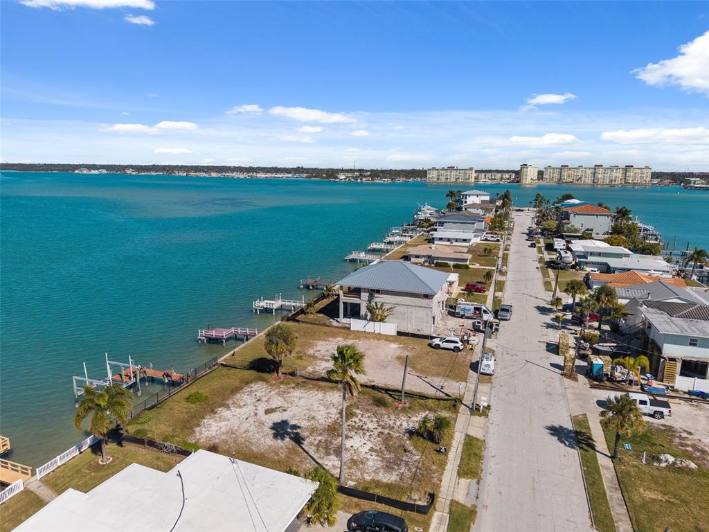 An aerial view shows waterfront homes and vacant lots along a street by the bay — 15307 HARBOR DRIVE, MADEIRA BEACH, FL