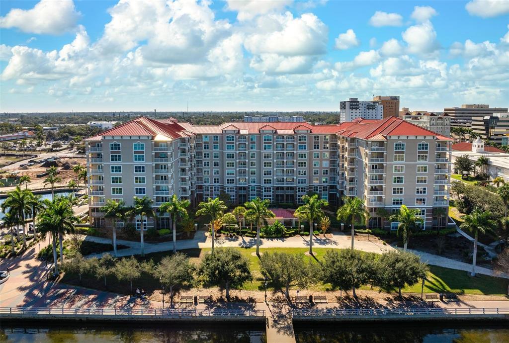 An aerial view shows a large, multi-story apartment building with a red roof near water — 808 3RD AVENUE W UNIT 402, BRADENTON, FL