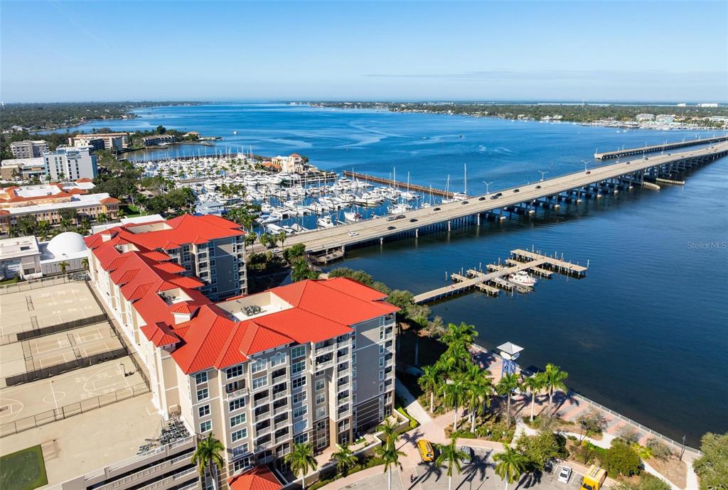 An aerial view shows a large waterfront building with a red roof next to a bridge — 808 3RD AVENUE W UNIT 402, BRADENTON, FL
