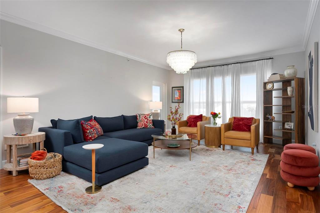 A living room features a blue sectional sofa, two tan armchairs, and a crystal chandelier — 808 3RD AVENUE W UNIT 402, BRADENTON, FL