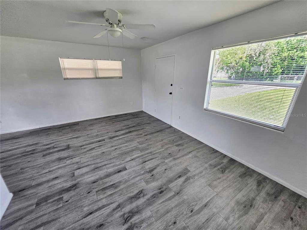 An empty room features gray wood-look flooring, white walls, a ceiling fan, and two windows — 185 E LAKE MARY AVENUE, LAKE MARY, FL