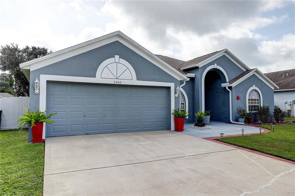 A blue single-story house features a two-car garage, a covered entryway, and a concrete driveway — 2242 TOWERING OAKS CIRCLE, SEFFNER, FL