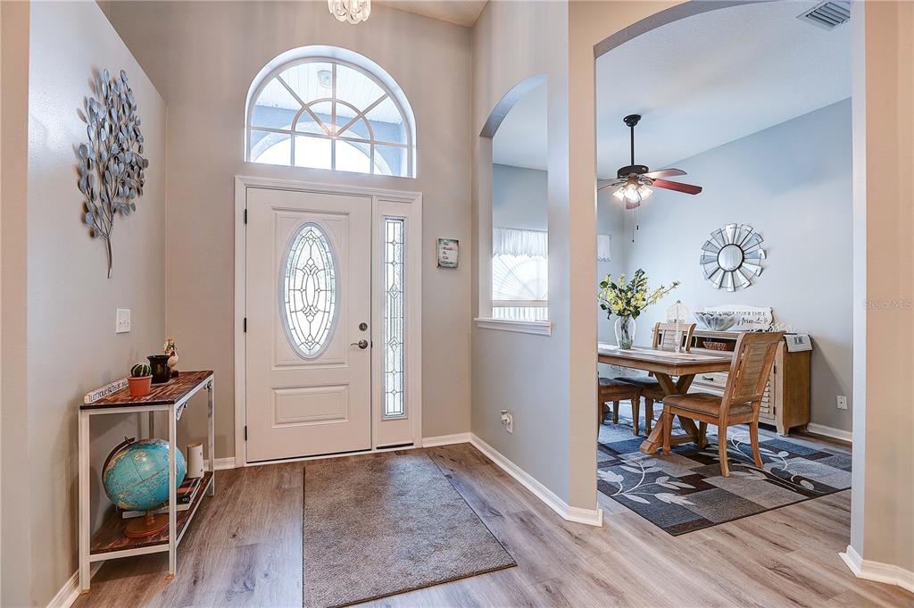 An entryway with a white front door, arched window, and wood-look flooring leads to a dining room — 2242 TOWERING OAKS CIRCLE, SEFFNER, FL