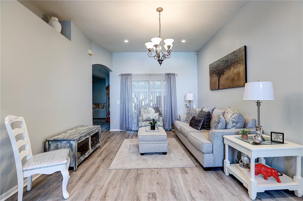 A living room features light wood-look flooring, a gray sofa, and a central chandelier — 2242 TOWERING OAKS CIRCLE, SEFFNER, FL