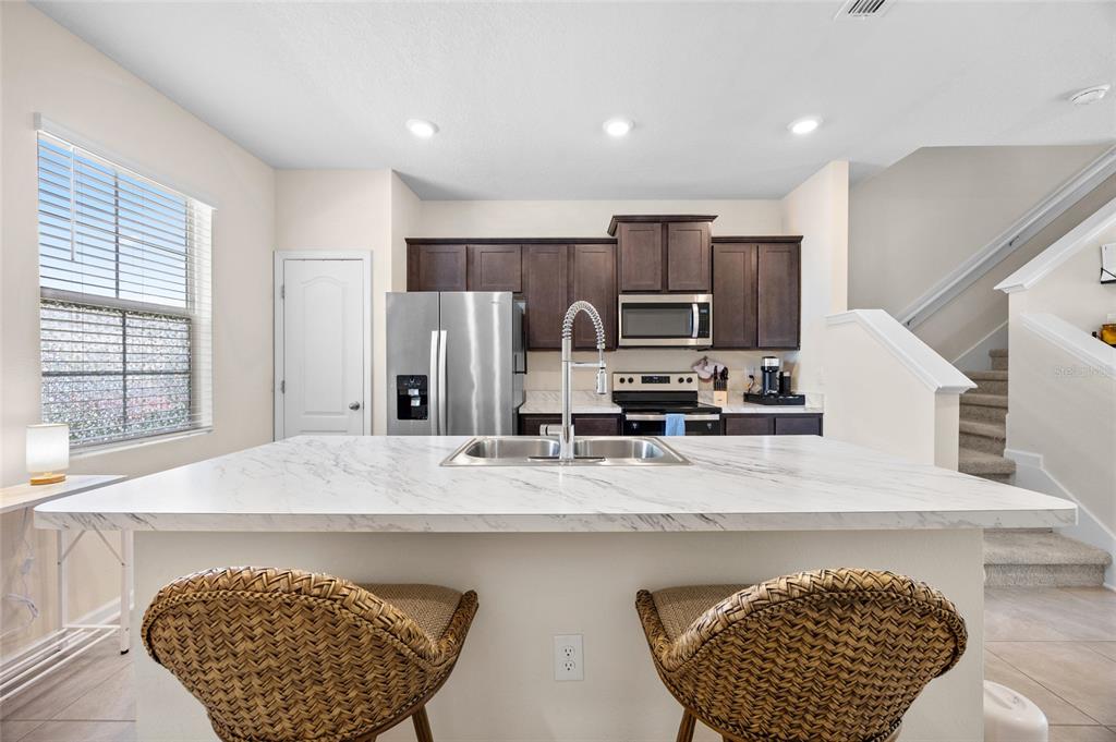 A kitchen with dark cabinets, stainless steel appliances, and a white marble-topped island — 585 RUNNING WOODS STREET, ORANGE PARK, FL