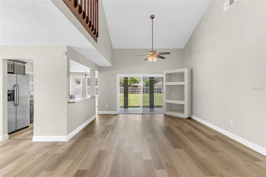 A living room with vaulted ceilings, wood-look flooring, a ceiling fan, and sliding glass doors — 12509 CRAYFORD AVENUE, ORLANDO, FL