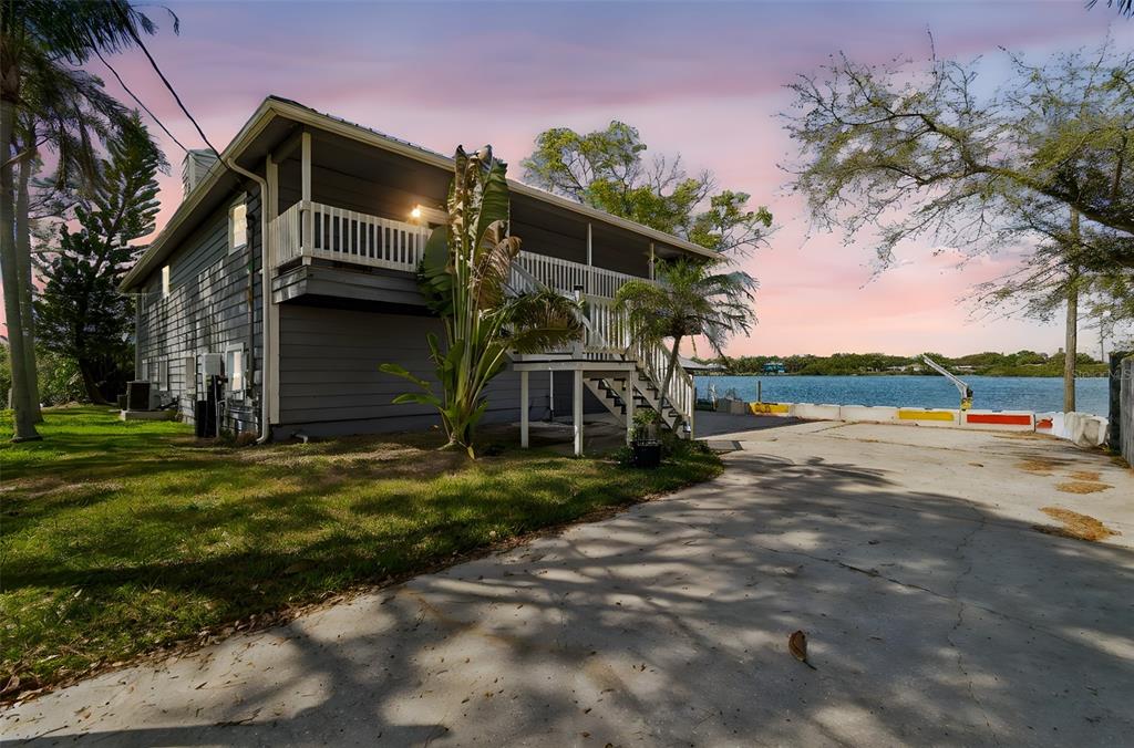 A two-story house with a balcony and stairs sits next to a concrete driveway by water — 9901 BAY DRIVE, GIBSONTON, FL