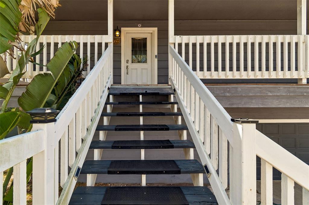 A set of wooden stairs with black treads leads up to a white front door — 9901 BAY DRIVE, GIBSONTON, FL